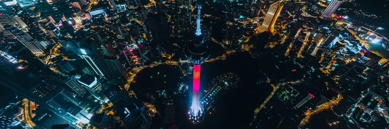 Aerial night view of Kuala Lumpur, Malaysia, with the illuminated KL Tower rising above a dense grid of city lights