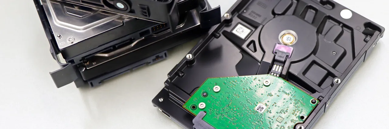 A stack of decommissioned bare hard disk drives on a white surface, one flipped to show its green circuit board and connectors